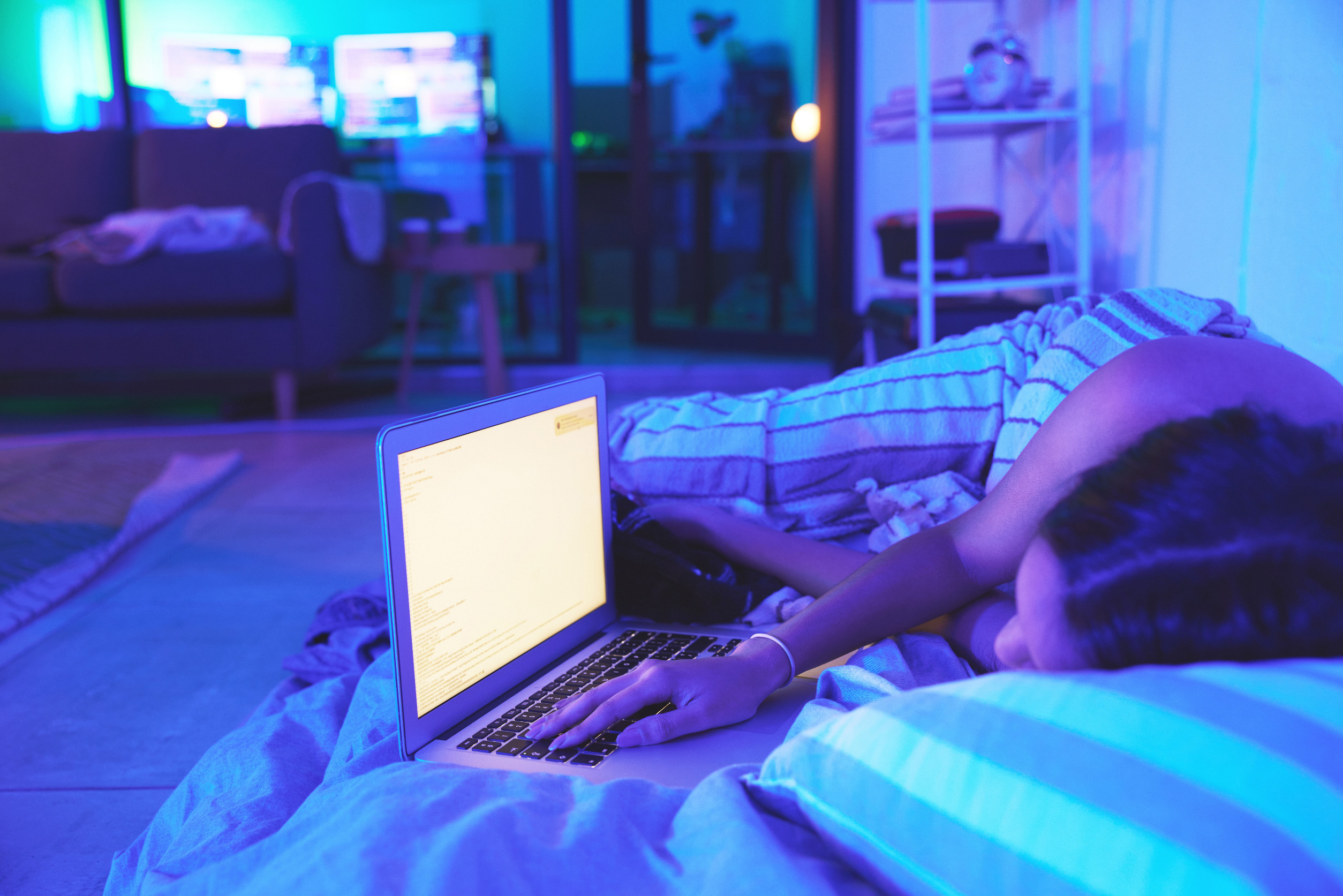 A women sleeping in a bed with a laptop next her, it's bright screen shining blue light